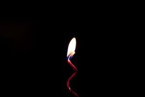 Vela roja encendida con forma ondulada sobre fondo negro, simbolizando calma, luz y minimalismo. Vela roja encendida con forma ondulada sobre fondo negro, simbolizando calma, luz y minimalismo.