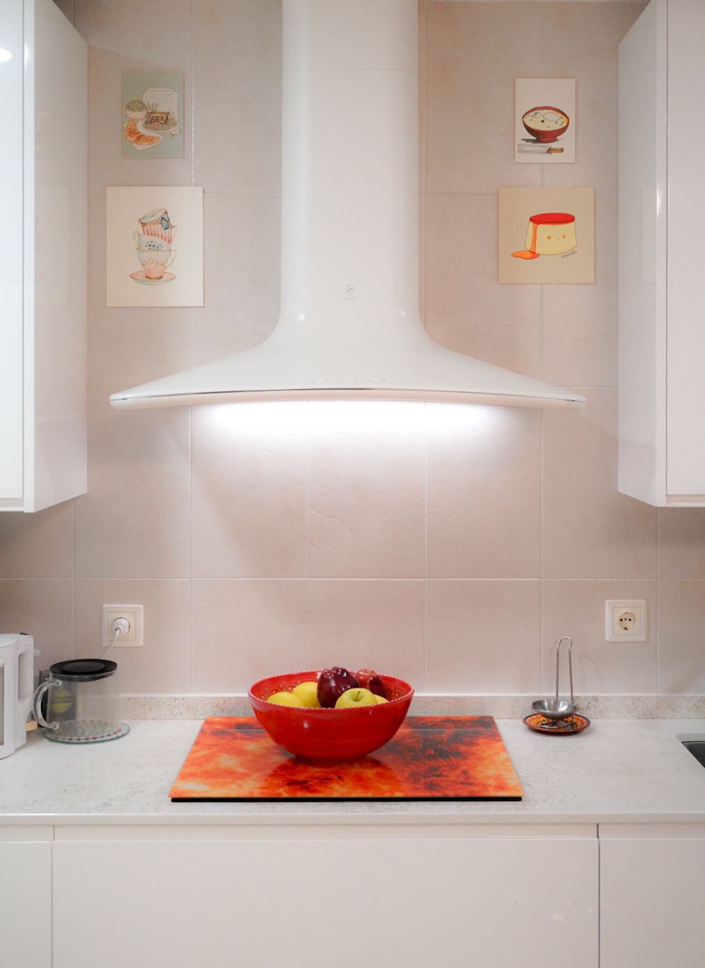 Cocina moderna y luminosa con campana extractora blanca, encimera clara y un cuenco rojo con frutas sobre una tabla decorativa. Cocina moderna y luminosa con campana extractora blanca, encimera clara y un cuenco rojo con frutas sobre una tabla decorativa.